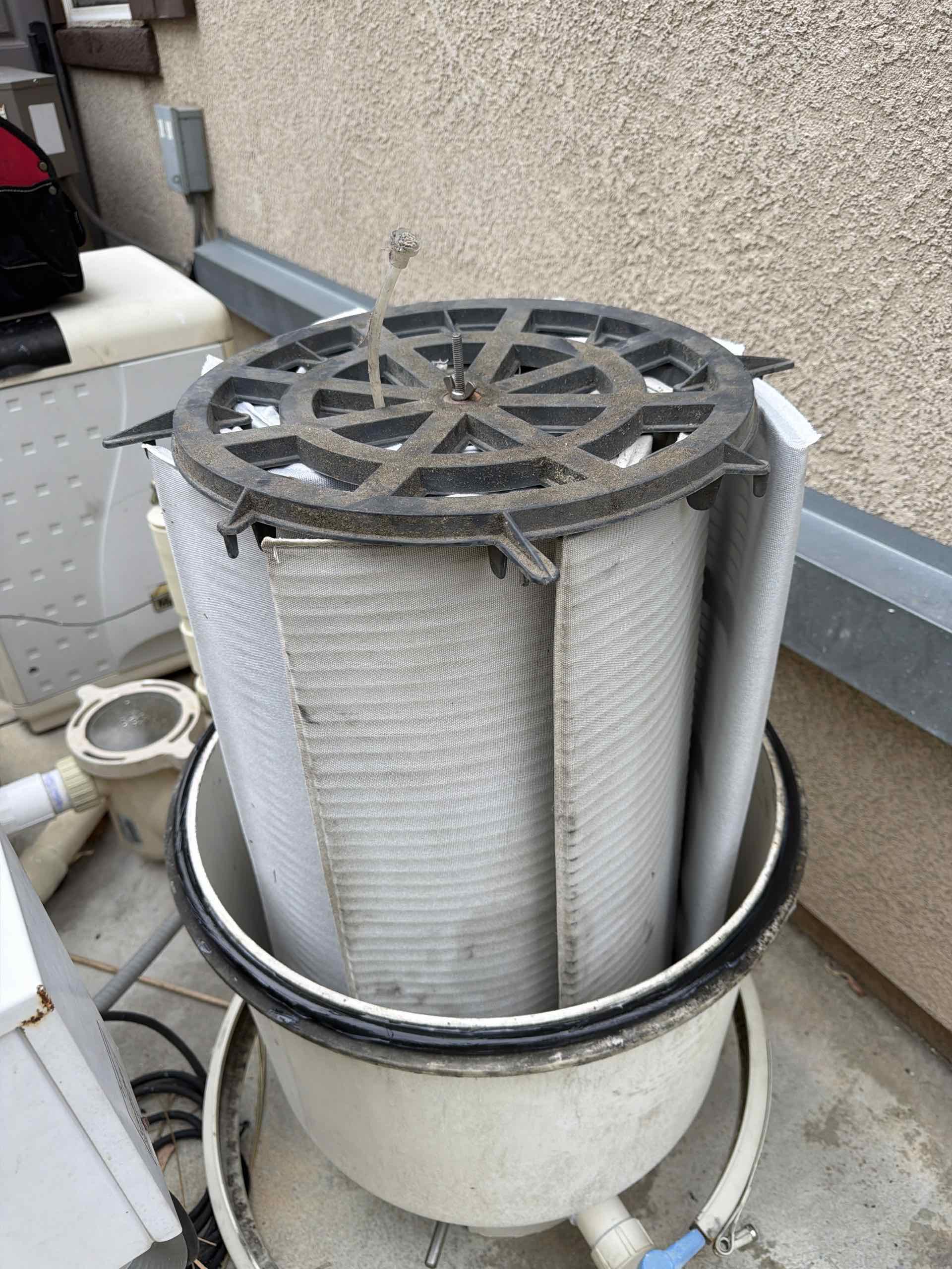 Outdoor pool filter system with a large round top and connected PVC pipes on a concrete deck