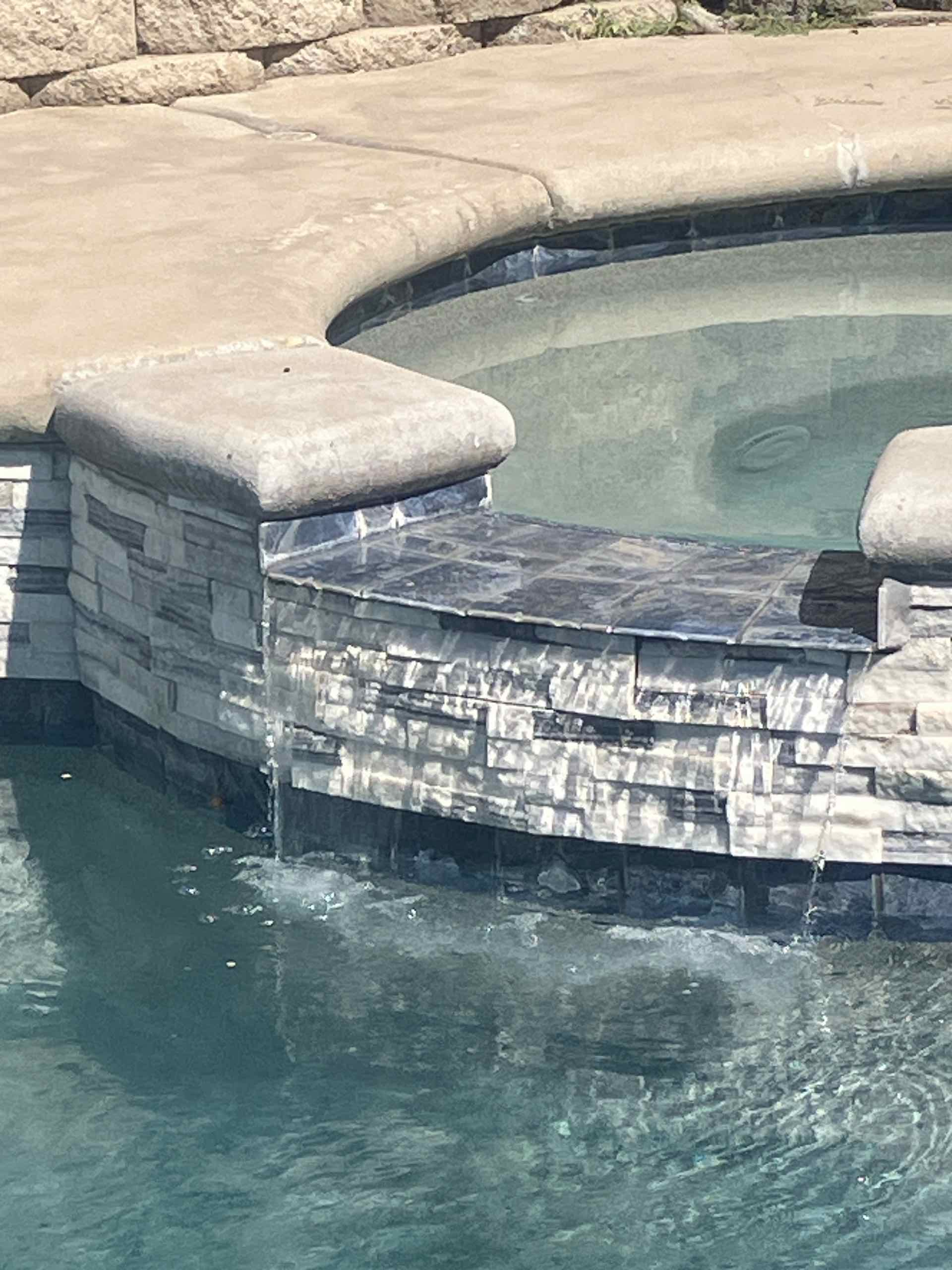 Stone pool edge with light gray coping and stacked stone wall, turquoise water below.