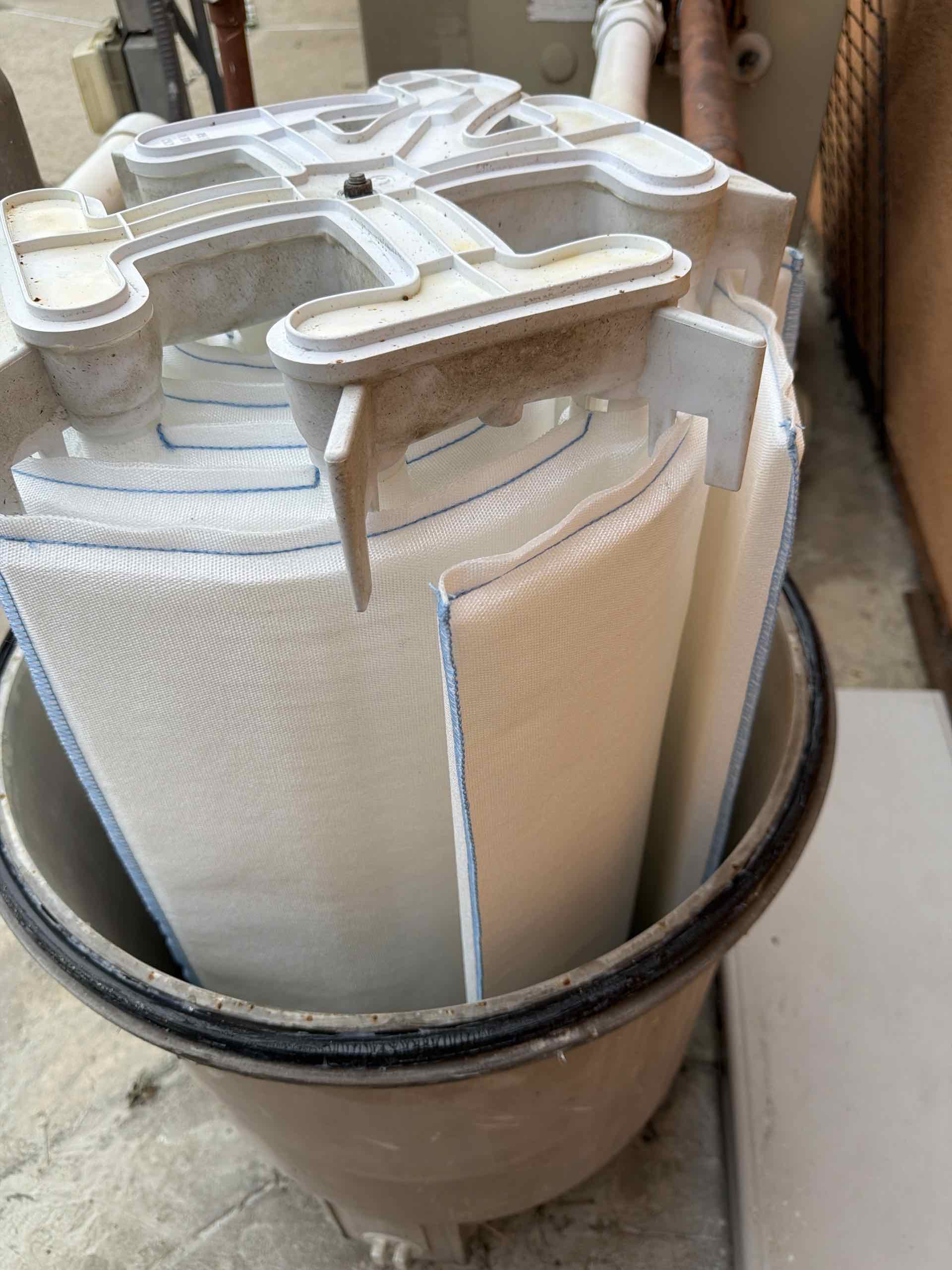 Close-up of a baghouse filter housing with white fabric filter bags installed inside a dusty industrial canister.