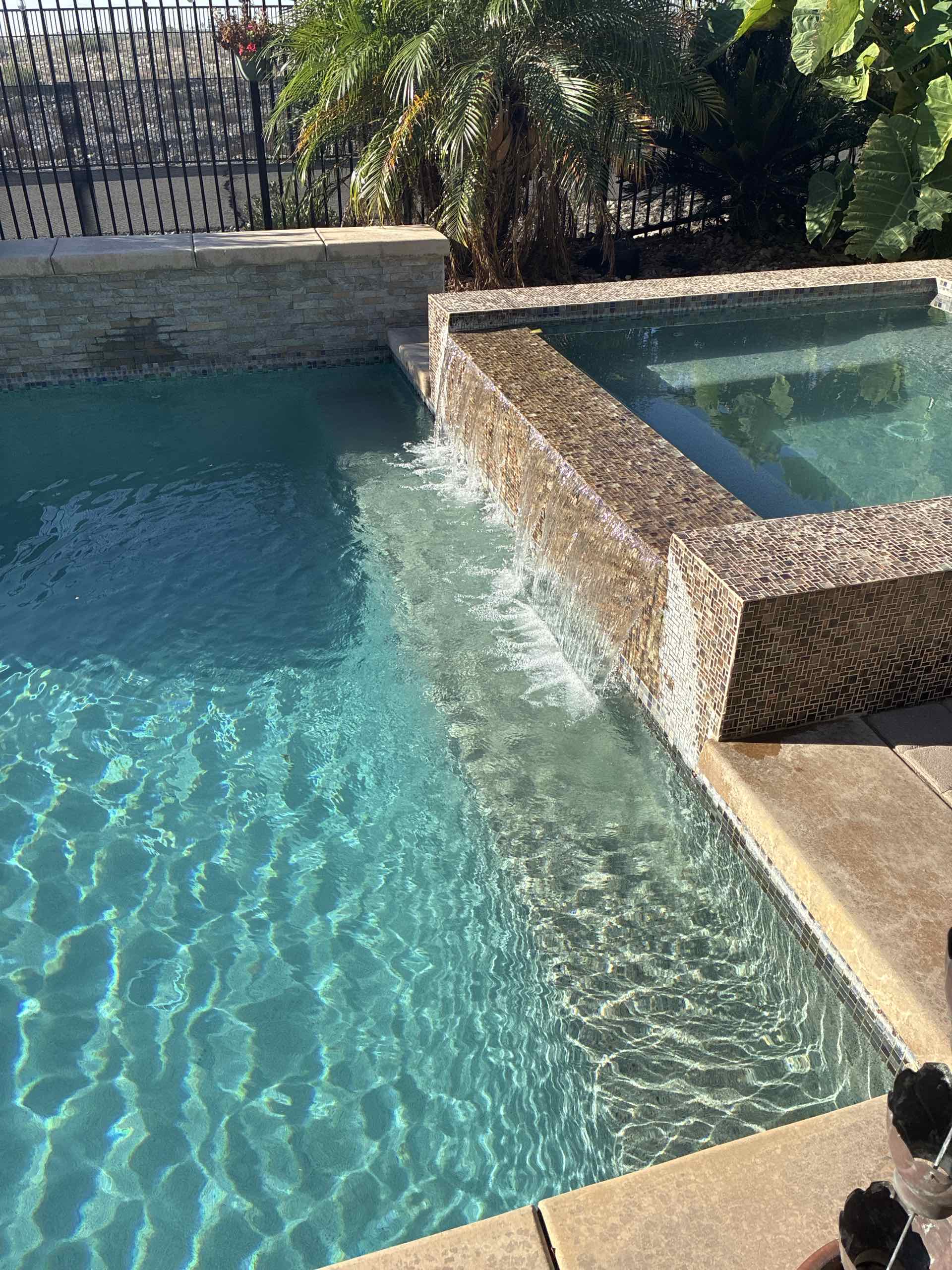 Swimming pool with turquoise water, a stone coping and a small cascading water feature creating ripples in the pool.